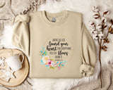 a beige sweatshirt with a floral design and text printed on it, along with a coffee mug and some decorative elements such as a snowflake and a branch.
