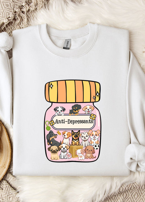 A white sweatshirt with a graphic design of a jar filled with various cartoon dogs and the text "Ani-Dependsents" printed on it. The sweatshirt is placed on a bed with a white blanket and a small white mug.