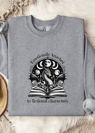 a gray sweatshirt with a graphic design on it, placed on a bed with a blanket and a mug.