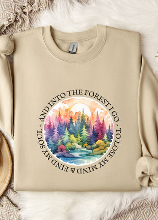 A beige sweatshirt with a colorful forest scene printed on it, along with a mug, a snowflake, and some cotton balls, all arranged on a white fur rug.