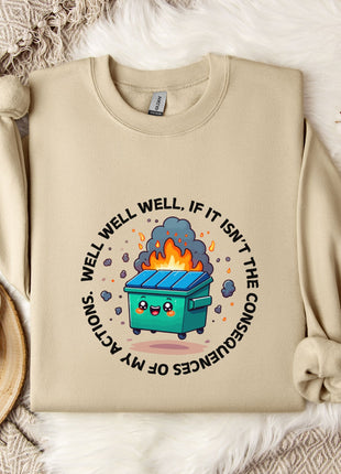 a beige sweatshirt with a graphic design depicting a fire-breathing trash can surrounded by flames and smoke. The sweatshirt is placed on a bed with a white blanket and a white mug.