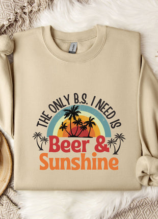 a beige sweatshirt with a graphic design that says "The only B.S. I need is Beer & Sunshine" along with a palm tree and sunset. The sweatshirt is laid out on a bed with a white blanket and a mug.