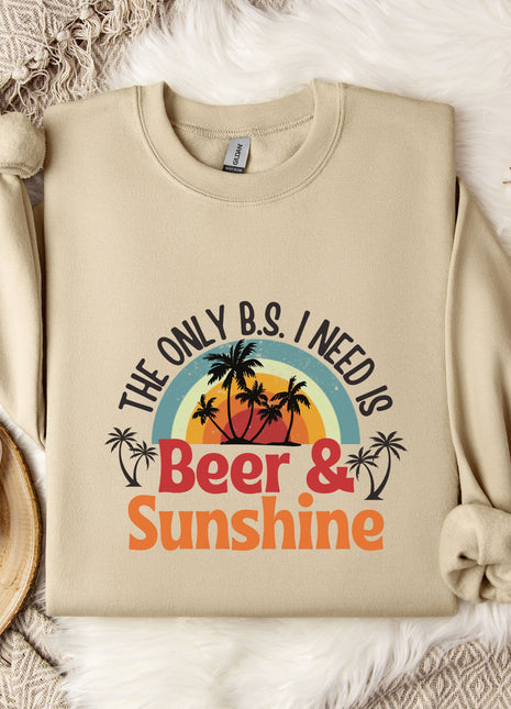 a beige sweatshirt with a graphic design that says "The only B.S. I need is Beer & Sunshine" along with a palm tree and sunset. The sweatshirt is laid out on a bed with a white blanket and a mug.