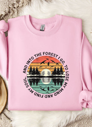 A pink sweatshirt with a graphic design depicting a sunset over a forest, surrounded by silhouetted trees and birds.