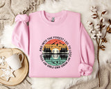 A pink sweatshirt with a graphic design depicting a sunset over a forest, surrounded by silhouetted trees and birds.