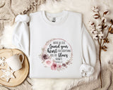 a white t-shirt with a floral design and text printed on it, placed on a bed with a white blanket and a white mug.