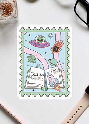 a colorful stamp with a whimsical illustration of a book, a rocket ship, and various other space-themed elements. The stamp is surrounded by various office supplies, including a pair of glasses, a pen, and a notebook.