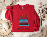 A red sweater with a graphic of a typewriter and flowers, along with the text "Emotionally Attached To Fictional Characters", is displayed on a bed with a white blanket and a white mug.