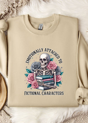 a beige sweatshirt with a graphic design depicting a skull surrounded by flowers and books, along with the text "Emotionally Attached to Fictional Characters".