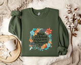A green sweatshirt with a floral design and text printed on it, along with a mug and some white flowers on a white surface.