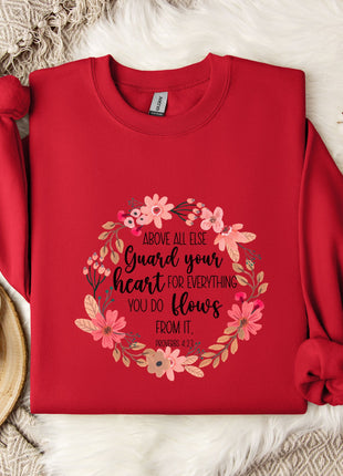 a red sweater with a floral design and text printed on it, placed on a white fur rug. There is also a white mug and a branch of cotton flowers nearby.