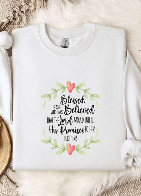 A white t-shirt with a printed text design, a white mug, and some white flowers on a bed with a white blanket.