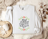 A white t-shirt with a printed text design, a white mug, and some white flowers on a bed with a white blanket.
