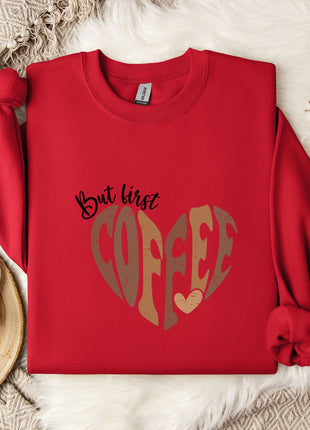 A red sweater with a heart-shaped design and the text "But first coffee" is displayed on a bed with a white blanket and a white mug with a heart-shaped design.
