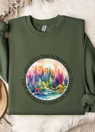 a green sweatshirt with a colorful forest scene printed on it, along with a mug and some white flowers on a bed.