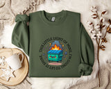 a green sweatshirt with a cartoon image of a fire-breathing trash can on it, along with the text "This little light of mine is shining to let me know it's coming".