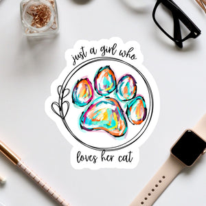 A sticker with a paw print and the text "Just a girl who loves her cat" is surrounded by various office supplies, including a pair of glasses, a pen, and a watch.