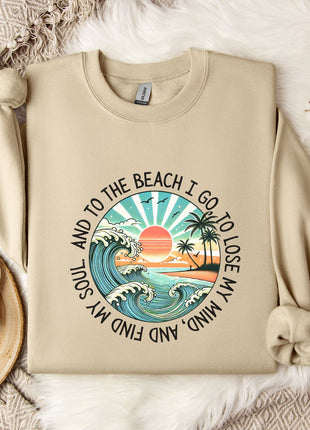 A beige sweatshirt with a graphic design depicting a beach scene, along with the text "And to the beach I go, I lose my soul and my mind".