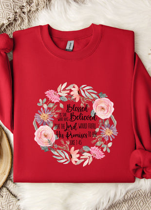 A red sweater with a floral design and text printed on it, along with a mug, a white mug, and some white flowers on a white fur rug.