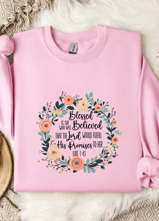 A pink sweatshirt with a floral design and text, placed on a white fur rug next to a white mug and a branch of cotton bolls.