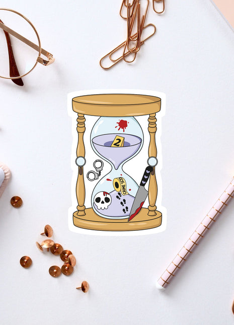 a sticker of an hourglass with a skull inside, surrounded by various office supplies such as pens, a notebook, and a pair of glasses.
