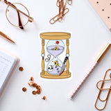 a sticker of an hourglass with a skull inside, surrounded by various office supplies such as pens, a notebook, and a pair of glasses.