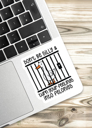 a sticker with a cartoon duck and the text "Don't Be Silly & Turn Your Feelings Into Felonies" placed on a laptop keyboard.
