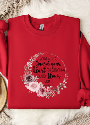 a red sweater with a floral design and text printed on it, placed on a white fur rug. There is also a white mug and a branch of cotton flowers nearby.