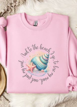 A pink sweatshirt with a seashell and starfish design, along with a mug and a branch of cotton bolls, all placed on a white fur rug.