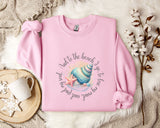 A pink sweatshirt with a seashell and starfish design, along with a mug and a branch of cotton bolls, all placed on a white fur rug.
