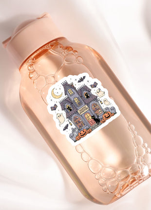 A pink bottle with a sticker depicting a spooky castle and Halloween decorations.