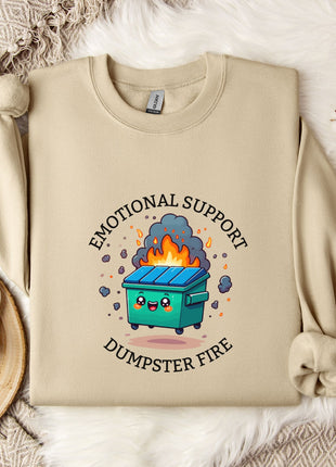 a beige sweatshirt with a graphic design depicting a dumpster with flames coming out of it, accompanied by the text "Emotional Support Dumpster Fire".