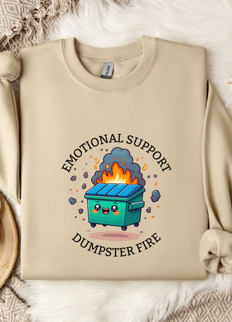 a beige sweatshirt with a graphic design depicting a dumpster with flames coming out of it, accompanied by the text "Emotional Support Dumpster Fire".