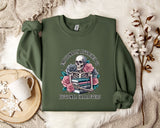 a green sweatshirt with a graphic design of a skeleton holding a book and flowers, accompanied by the text "I DON'T CARE ABOUT ANYTHING" and "FICTIONAL CHARACTERS".