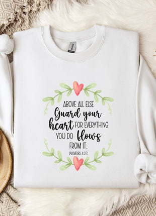 a white t-shirt with a printed message, a white mug, and some white flowers on a bed with a white blanket.