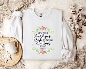a white t-shirt with a printed message, a white mug, and some white flowers on a bed with a white blanket.