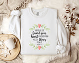 a white t-shirt with a printed message, a white mug, and some white flowers on a bed with a white blanket.