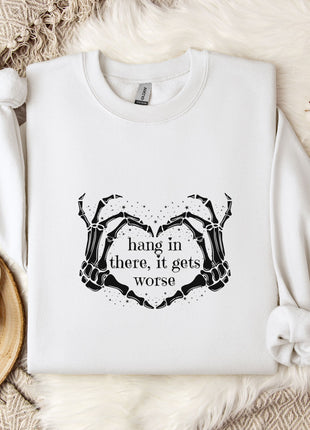 A white sweatshirt with a graphic design and text printed on it, along with a mug, a branch of cotton bolls, and a wooden tray with snowflakes on it, all arranged on a white fur rug.