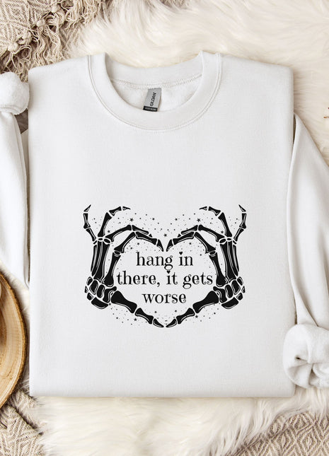 A white sweatshirt with a graphic design and text printed on it, along with a mug, a branch of cotton bolls, and a wooden tray with snowflakes on it, all arranged on a white fur rug.