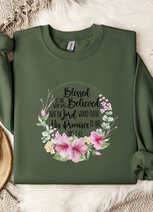 A green sweatshirt with a floral design and text printed on it, placed on a white fur rug. There is also a white mug and some white flowers in the background.