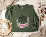 A green sweatshirt with a floral design and text printed on it, placed on a white fur rug. There is also a white mug and some white flowers in the background.