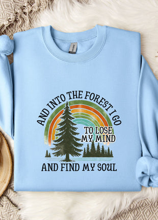 A light blue sweatshirt with a graphic design of a forest and a rainbow, along with the text "And into the forest I go, to lose my mind and find my soul".