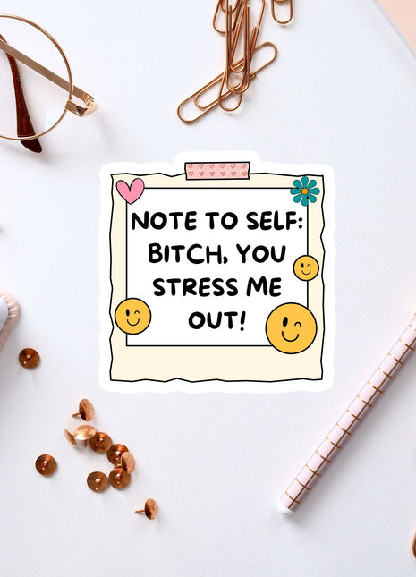a white sticker with a message, surrounded by various office supplies and items such as a pen, a pair of glasses, and a notebook.