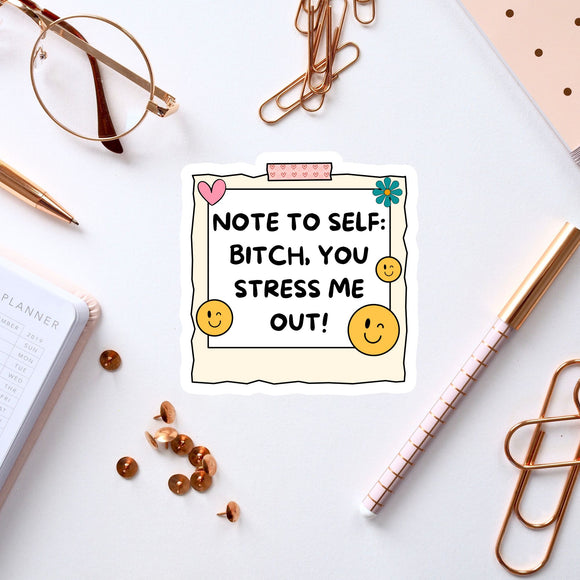 a white sticker with a message, surrounded by various office supplies and items such as a pen, a pair of glasses, and a notebook.