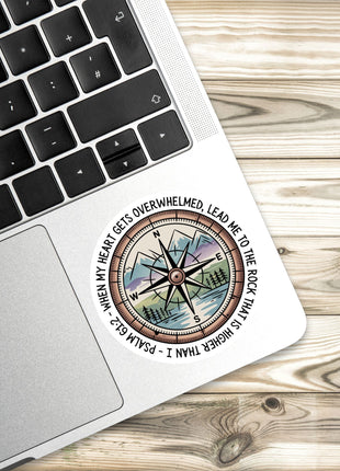 A sticker with a compass and a Bible verse is placed on a laptop keyboard.