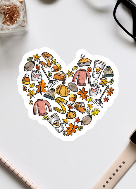 A heart-shaped sticker with various fall-themed items such as pumpkins, leaves, and sweaters, along with a pair of glasses and a watch, all arranged on a white background.