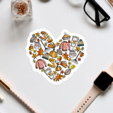 A heart-shaped sticker with various fall-themed items such as pumpkins, leaves, and sweaters, along with a pair of glasses and a watch, all arranged on a white background.