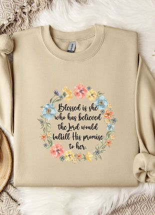 A beige sweatshirt with a floral wreath design and a quote printed on it, along with a mug, a white flower, and some cotton balls on a white fur-covered surface.