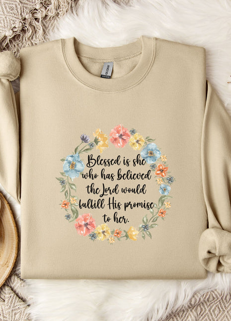 A beige sweatshirt with a floral wreath design and a quote printed on it, along with a mug, a white flower, and some cotton balls on a white fur-covered surface.