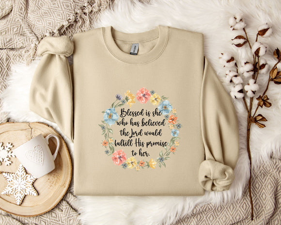 A beige sweatshirt with a floral wreath design and a quote printed on it, along with a mug, a white flower, and some cotton balls on a white fur-covered surface.